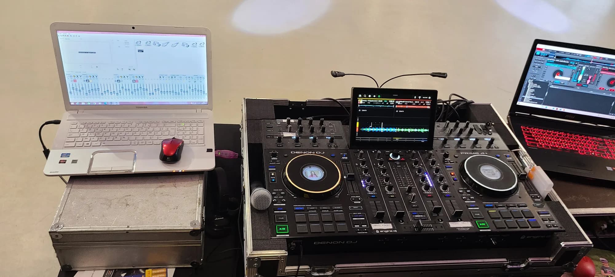 Console DJ Denon Prime 4 encadrée de deux ordinateurs portables et d'un micro, posée sur un flight case