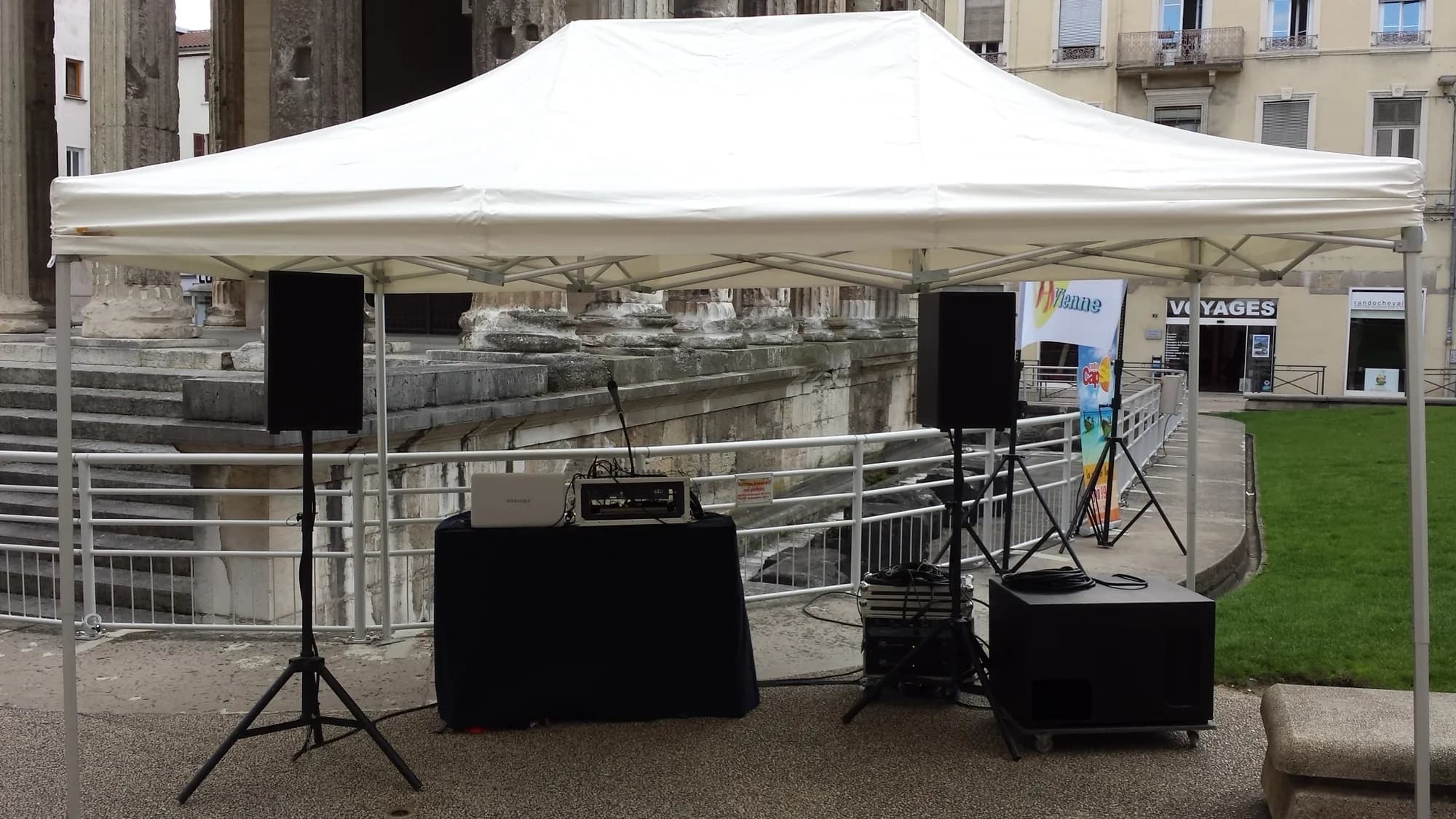 Barnum blanc abritant deux enceintes sur pieds, un caisson de basses et une console DJ, devant le temple romain de Vienne