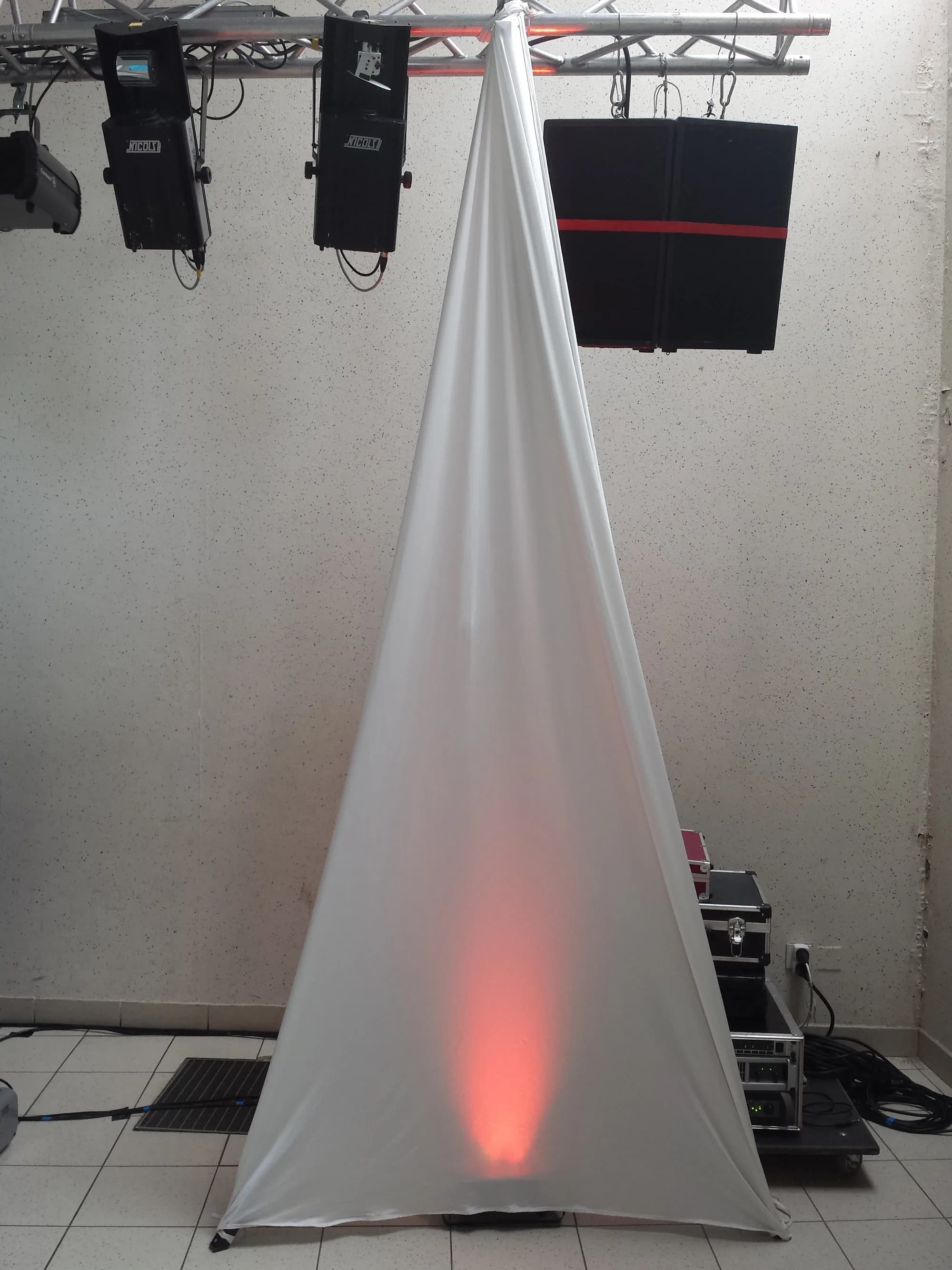 Structure en poutres d'aluminium tendue d'un drapé blanc éclairé en rouge, entourée de projecteurs et de flight cases
