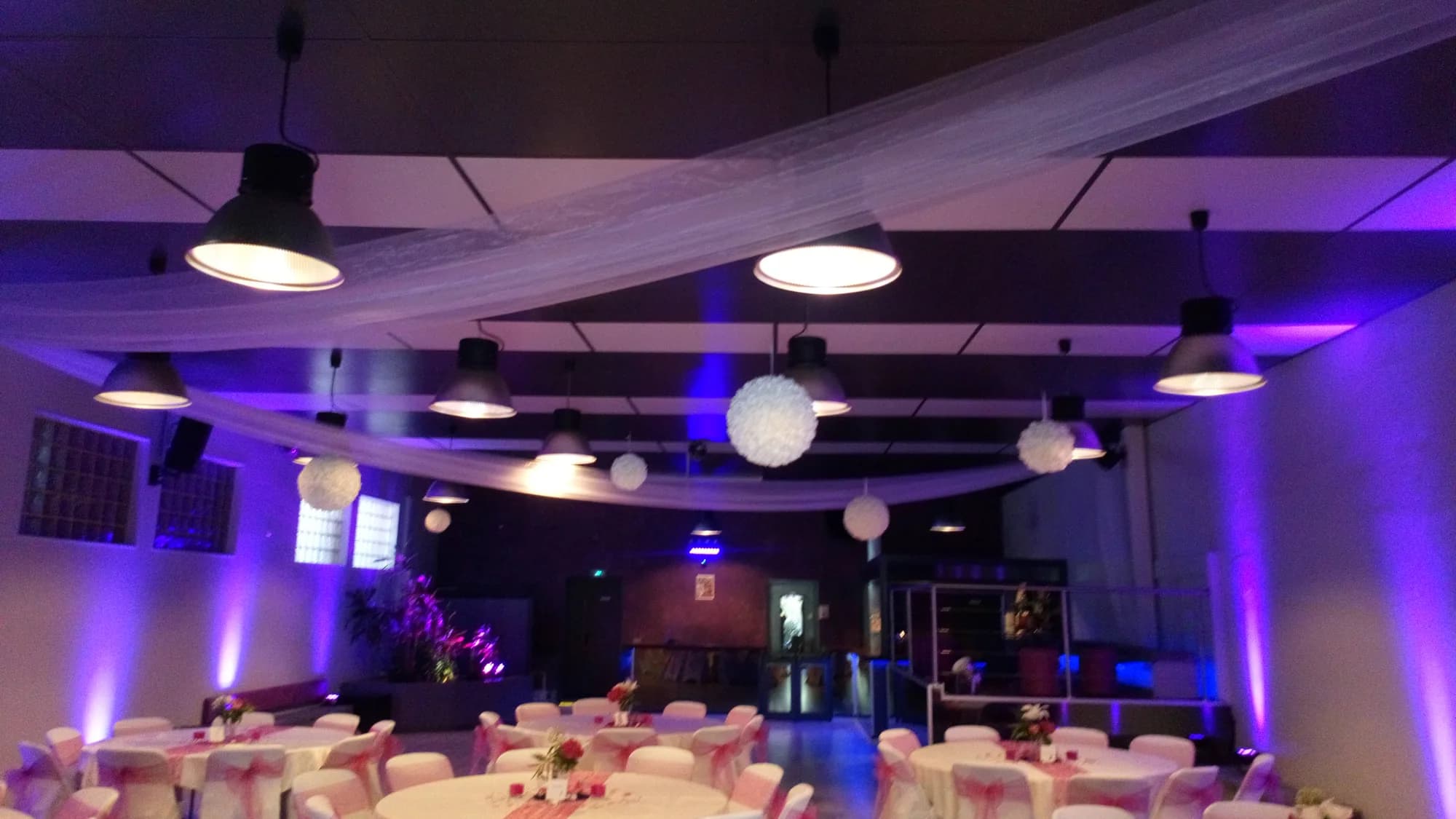Grande salle au plafond tendu de voilages blancs et de boules de papier, murs éclairés en violet et bleu