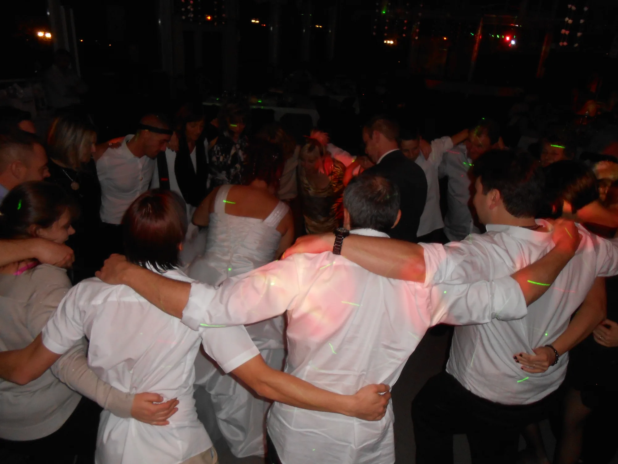 Ronde d'invités bras sur les épaules autour de la mariée en robe blanche, sur la piste de danse