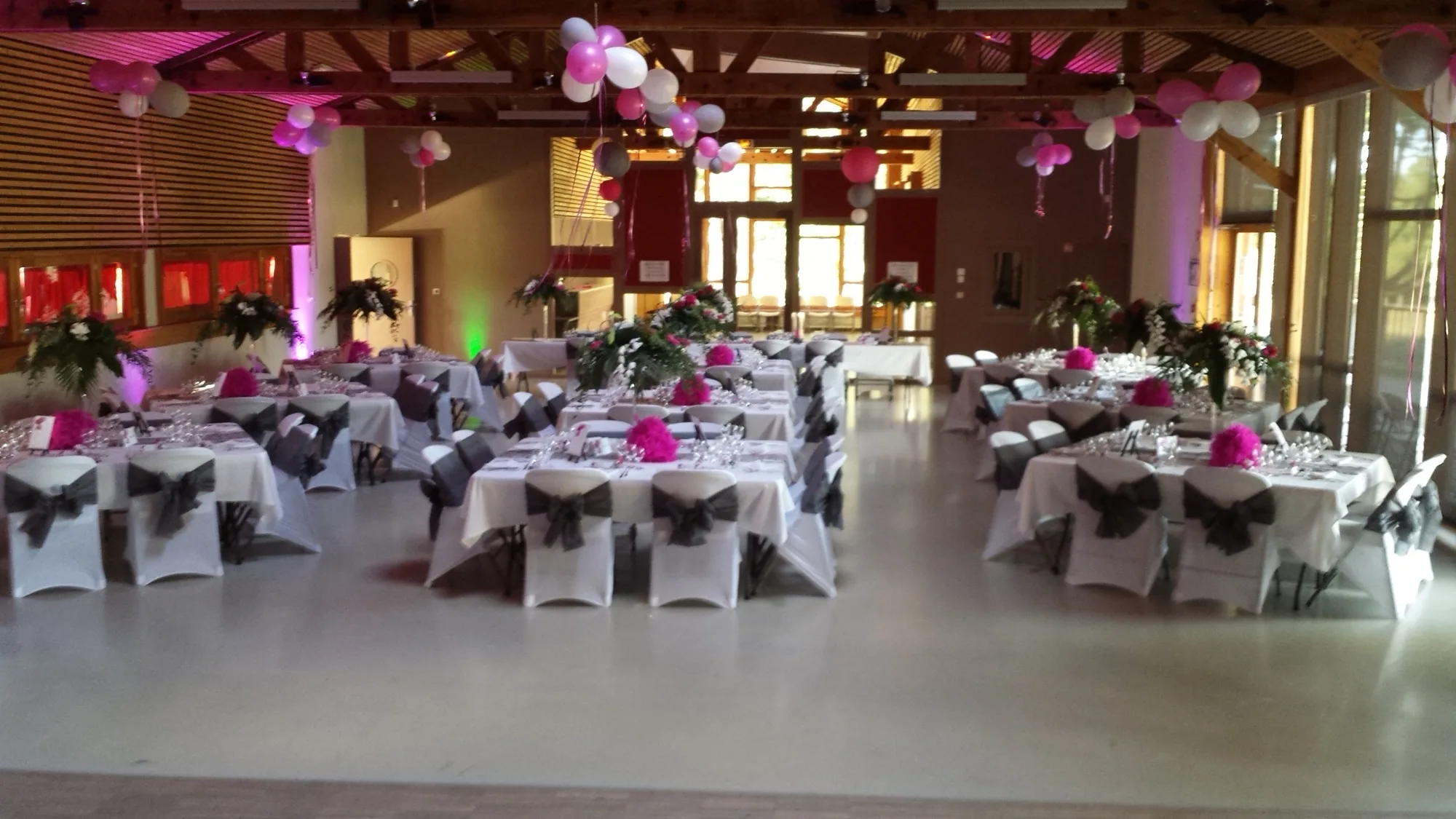 Salle des fêtes décorée d'arches de ballons fuchsia et blancs, tables dressées autour d'une piste de danse vide