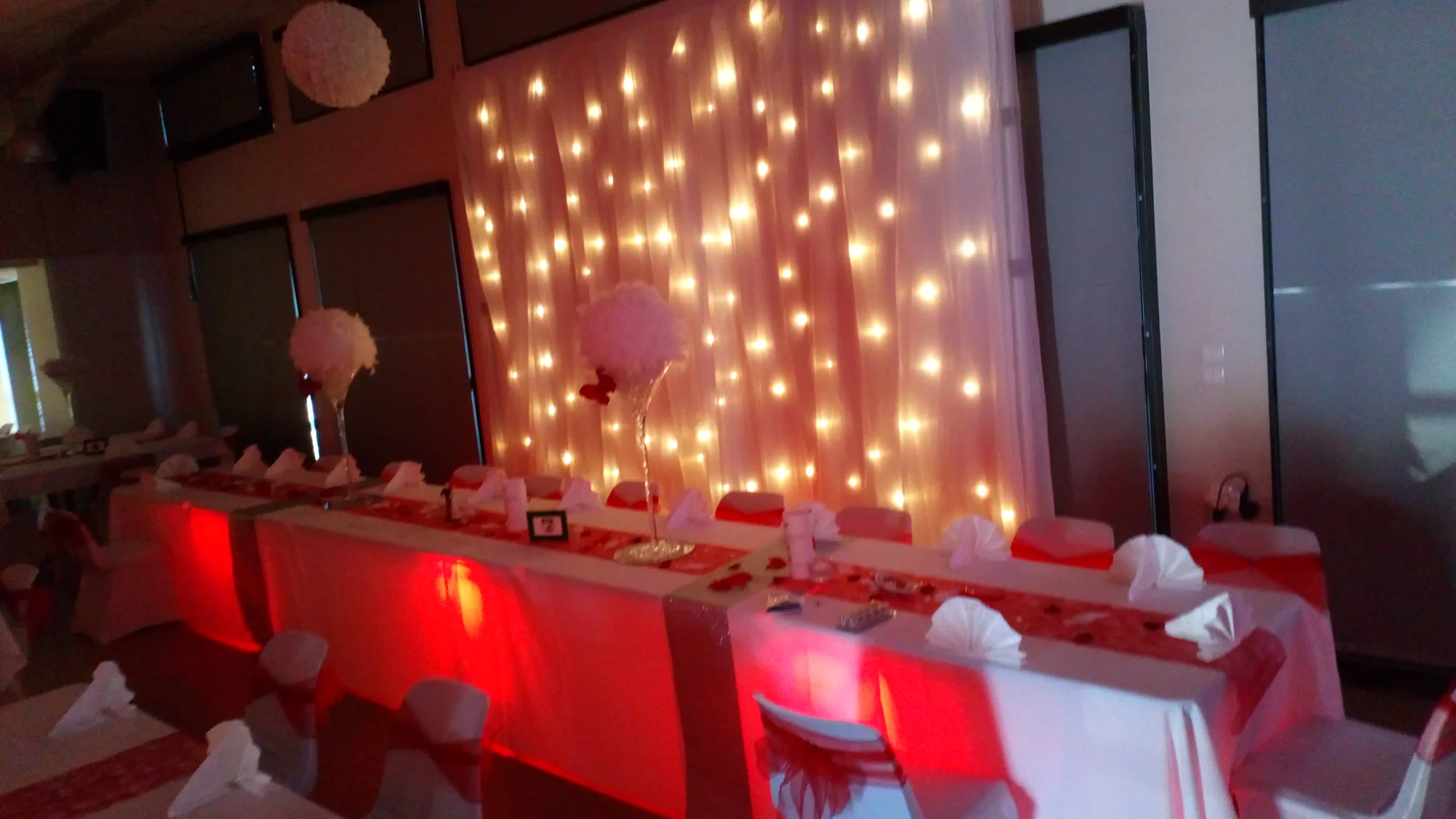 Table d'honneur habillée de rouge et de blanc devant un rideau de guirlandes lumineuses